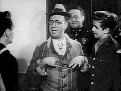a man in what appears must be a brightly colored suit and hat, as this is a black and white photo, is the centre of attention speaking to three young men