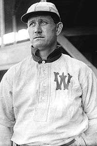 A man, wearing a baseball cap and a white baseball uniform with the letter "W" on the left breast, faces forward towards the left.