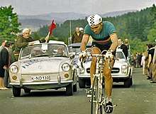 A man on a bicycle, with a car behind him.