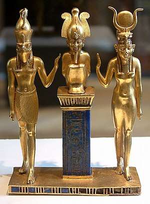 Gold statuette of three human figures. On the right is a woman with a horned headdress, in the center is a squatting man with a tall crown on a pedestal, and on the left is a man with the head of a falcon.