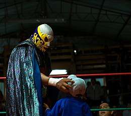 A picture of the masked wrestler El Canek giving a young fan an autograph.