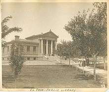 An old photograph of a large building with a pathway lined by trees leading to it