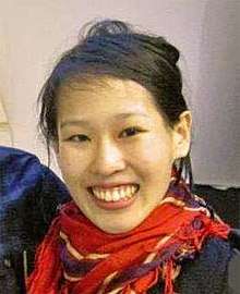 A smiling Asian woman wearing a red scarf and black coat