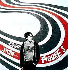A man (Elliott Smith), rendered in black-and-white, stands in front of a wall with a white background and four big swirly lines of paint forming an 'S' shape behind him; the first two are black, the third is red, and the last is black. "Elliott Smith ••" and "Figure 8" are written in white text on the swirls to the left and right sides of the man, respectively.