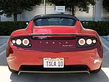 Photograph of a parking space with the words "SpaceX" and "reserved".  The parking space contains a red convertible sports car with Californian license plate TSLA 10. On the rear of the vehicle are written the words "Tesla Roadster Sport".