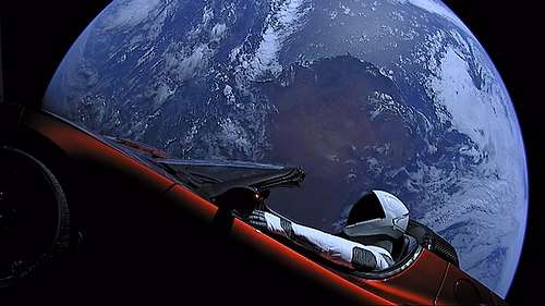 Large circular disc of a fully-illuminated planet Earth floating in the blackness of space. In front of Earth is a red convertible sports-car seen from the side. A humanoid figure wearing a white-and-black spacesuit is seated in the driving seat with the right-arm holding the steering wheel, and the left-arm resting on the top of the car door.