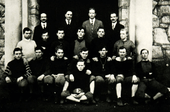 An old black and white photograph of eighteen male student members dressed in football gear