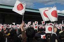 A group of people wave Japanese flags at a palace.