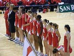 English national team is standing in a row, wearing red uniforms, on one of the centre lines that divides the court in three.