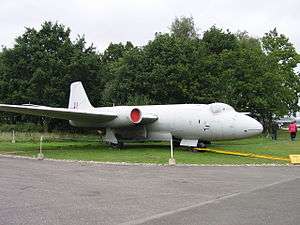 Front three-quarter view of white twin-engined military jet parked on grass