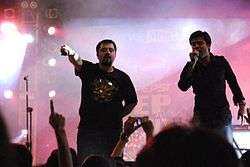 Khan and Ahmed Ali Butt onstage; Khan is singing, and Butt is holding his microphone to the audience
