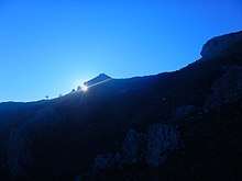 blue sky and sun setting behind mountain
