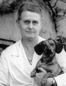 Outdoor portrait of Mohr in a white lab coat, holding a dachshund in one arm