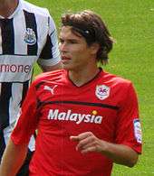 A young footballer, with long hair and in a red jersey, standing in front of his opponent during a football match between Cardiff City and Newcastle United.