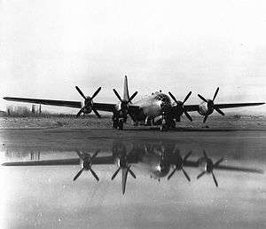 Black and white photo of a military aircraft powered by four propeller engines parked in an open area