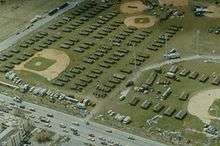 Aerial view of a large number of temporary housing tents positioned throughout several baseball fields