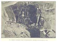 Inside a gold mine; men stand in a rough underground passage.