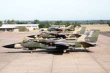 Side view of jets in two-tone green camouflage livery parked side-by-side on ramp.