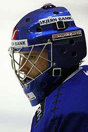A side shot of an ice hockey players head and shoulder. He is wearing a blue helmet and uniform.