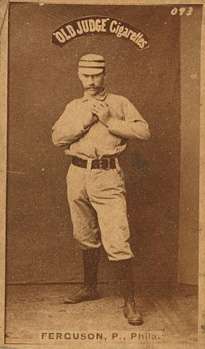 A baseball-card photograph of a mustachioed man in an old-style white baseball uniform holding a baseball in front of his chest with both hands