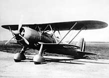 A black and white photograph of a single-propeller biplane on the ground