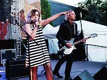 Corin Tucker pointing and holding a microphone beside Peter Buck playing guitar