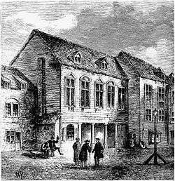 A three-story building with three men standing in front having a conversation, and one or more other people near the building.