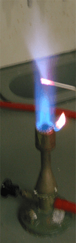 A flame with a small metal rod penetrating it; the flame near the rod is pale blue.