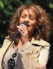 A picture of a woman with brown curly hair wearing a jacket, singing