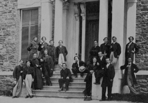 A group of men assembled on the front steps of a building, posed in formal wear.