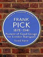 A circular blue ceramic plaque with white raise lettering fixed to a brick wall bears the text "FRANK PICK, 1878-1941 Pioneer of Good Design for London Transport lived here"