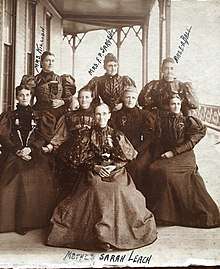 Eight women in Victorian-style dresses posing for a photo in front of a building. The woman in front and center is labeled with handwriting as "Mother Sarah Leach". The remaining seven woman form two rows behind Mrs. Leach. The three woman in the back row are also labeled in handwriting from left to right, "Mrs. Killion, Mrs. F.P. Sargent, and Mrs. E.A. Ball".
