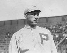 A black-and-white image of a man wearing an old-style baseball uniform with a "P" on the chest and a white crownless baseball cap