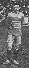 A black and white photograph of a man in a football kit standing on a grass pitch.