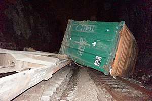 A large green metallic container lying on its side across some railroad tracks, one corner resting on a concrete structure on the left, seen at night.