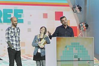 Three people, two women and a man, stand on an awards stage with a podium.