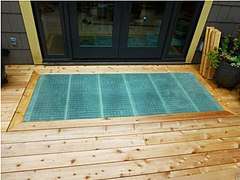 Pine decking with a panel of fiberglass showing a fine grid set in a mitered pine frame. The fiberglass is slightly blue-green, and sits squarely in front of the glass doors to the house.
