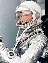 Glenn in a silver spacesuit, with his helmet on and clear visor down