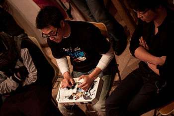GamerBee is shown from above, focusing on a match while using an arcade stick resting on his lap