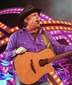 Garth Brooks performing on stage, while holding a guitar.