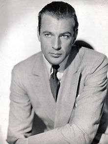 Black and white photo of Gary Cooper in 1936—a handsome white man, light-eyed with hair combed back, wearing a light-colored suit and around 30 years of age.