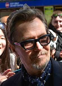 Photo of the 2018 recipient of the Best Actor award: Gary Oldman—a white male from England pictured in 2014 at 56 years of age, with brown hair brushed up and back, a salt-and-pepper goatee, wearing eyeglasses and a dark suit jacket with a white shirt.