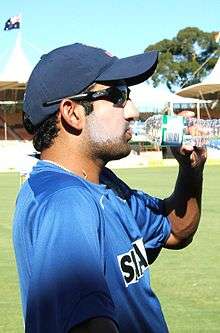 A man wearing Indian training jersey and drinking from bottle