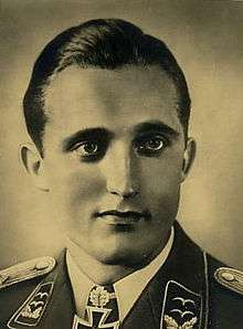 The head and shoulders of a young man, shown in semi-profile. He wears a military uniform with an Iron Cross displayed at the front of his white shirt collar.
