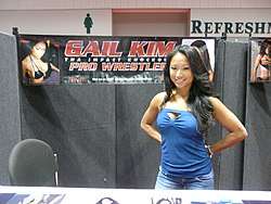 An Asian female with dark hair wearing light-blue wrestling gear standing in front of a crowd.