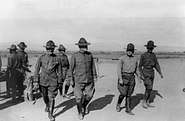 Three men in military uniform in the foreground, dressed in U.S. Army Uniforms appropriate for 1916.