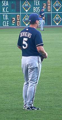 A man in a navy-blue baseball jersey and cap and gray baseball pants stands on a baseball field.