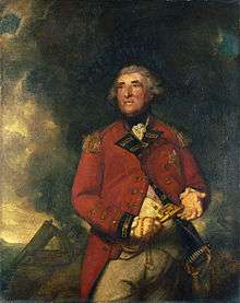 An portly English officer with a ruddy complexion and black eyebrows, stands in military dress against a background of smoke from a cannon. He holds a very large key in one hand and gestures with the other.