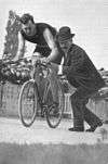 A picture of George Leander being pushed on a bike by someone.