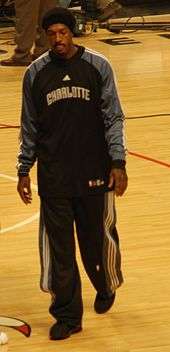 A black person wearing a black team jacket and pants walking on a basketball court